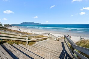 A wooden boardwalk leading to a beach with a clear view of the ocean and distant mountains.