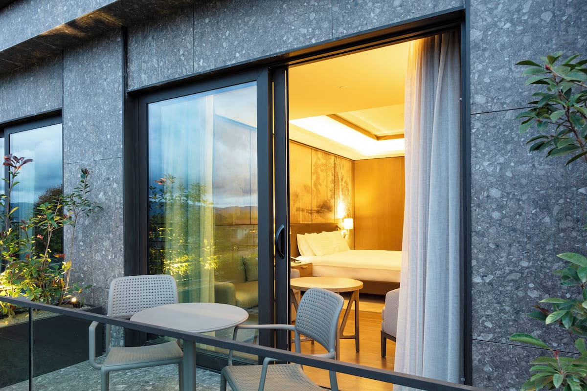 Ein modernes Hotelzimmer mit Glastür zu einem Balkon, einem Bett, einem kleinen Tisch und zwei Stühlen.