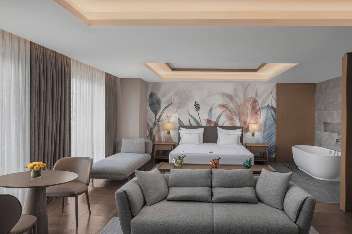 Ein modernes Hotelzimmer mit einem Bett, zwei Sofas, einem Couchtisch, einem Schreibtisch und einer Badewanne.