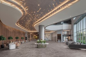 Un hall d’entrée spacieux avec un comptoir d’accueil central, des espaces de détente et un design moderne au niveau du plafond.