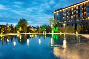 Un hotel moderno con piscina, rodeado de árboles iluminados y un cielo nocturno despejado.
