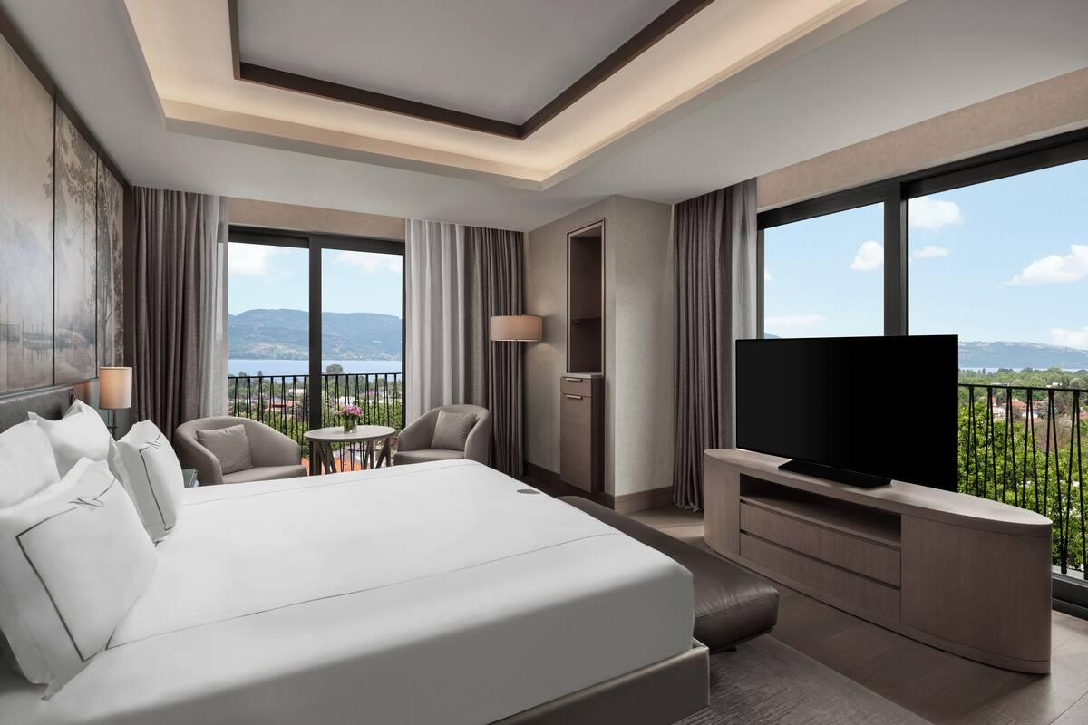 Ein modernes Hotelzimmer mit einem großen Bett, einem Flachbildfernseher, einem Schreibtisch und einem Balkon mit Bergblick.