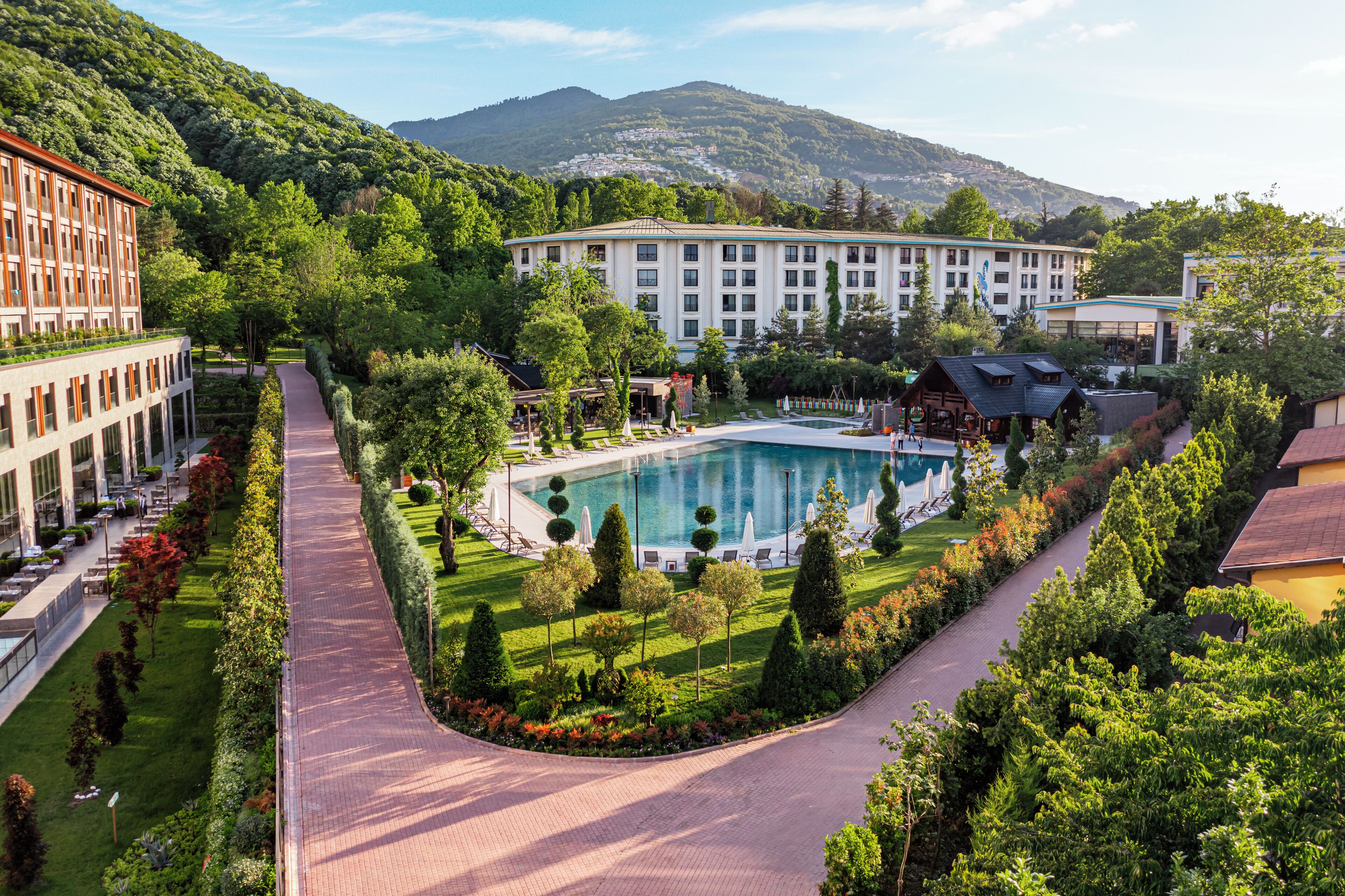 A resort with a swimming pool, manicured gardens, and a mountainous backdrop.