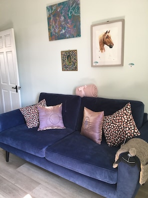 A dark blue sofa with patterned cushions, a rolled blanket, and a stuffed animal.