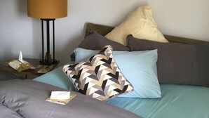 Una cama bien hecha con varias almohadas, una mesita de noche con lámpara y dos cuadros florales en la pared.