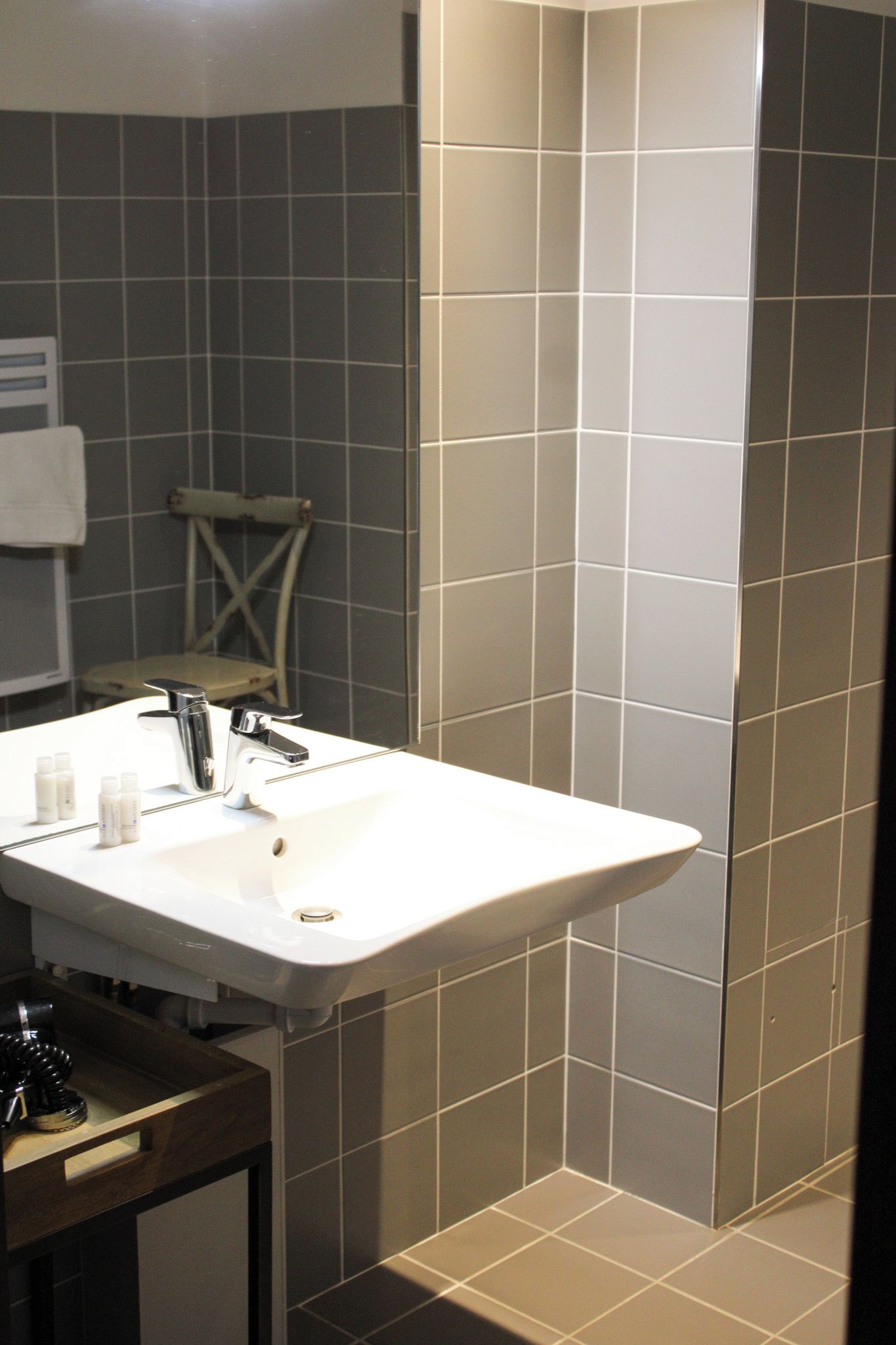 Un baño con lavamanos blanco, espejo y paredes con azulejos.