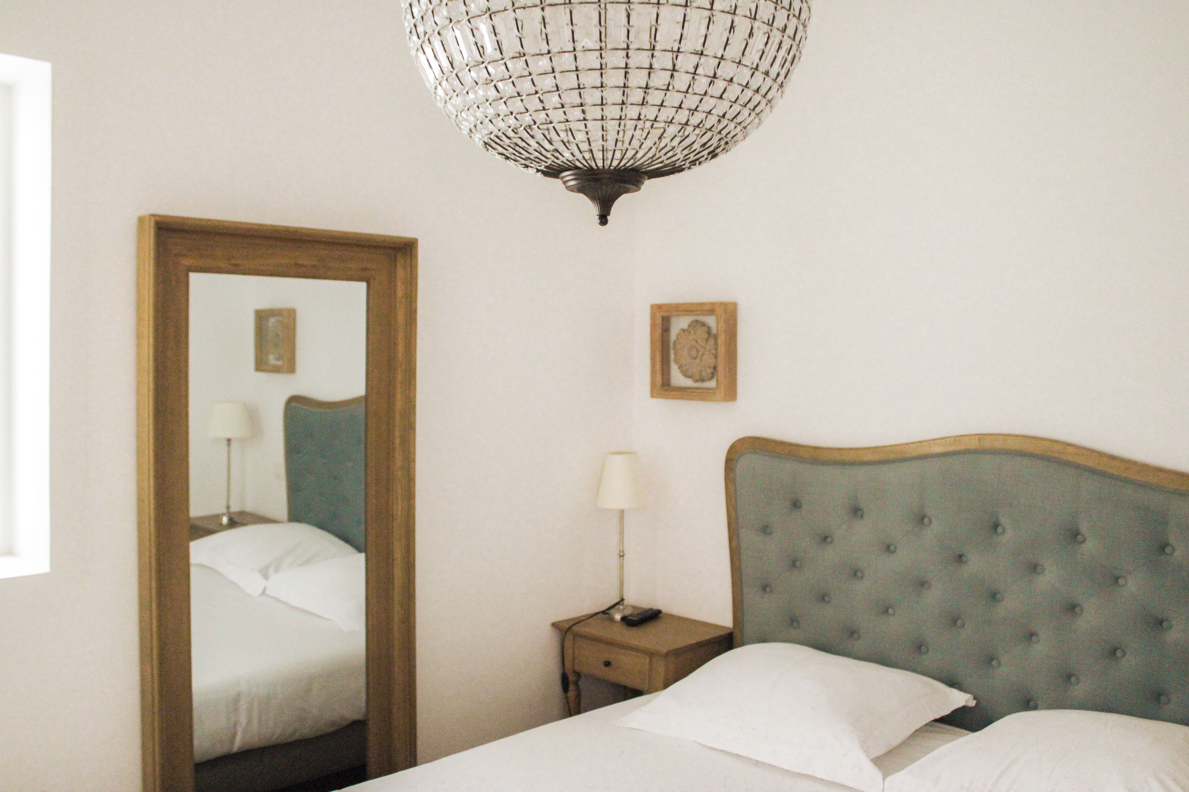 Un dormitorio con cama, mesita de noche, lámpara, espejo y candelabro.