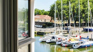 Vista desde una ventana con vista a un puerto deportivo con barcos amarrados, un paseo marítimo pavimentado y un edificio al fondo.