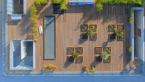 Vista aérea de una terraza en la azotea con varias zonas de estar, jardineras y una fuente central.