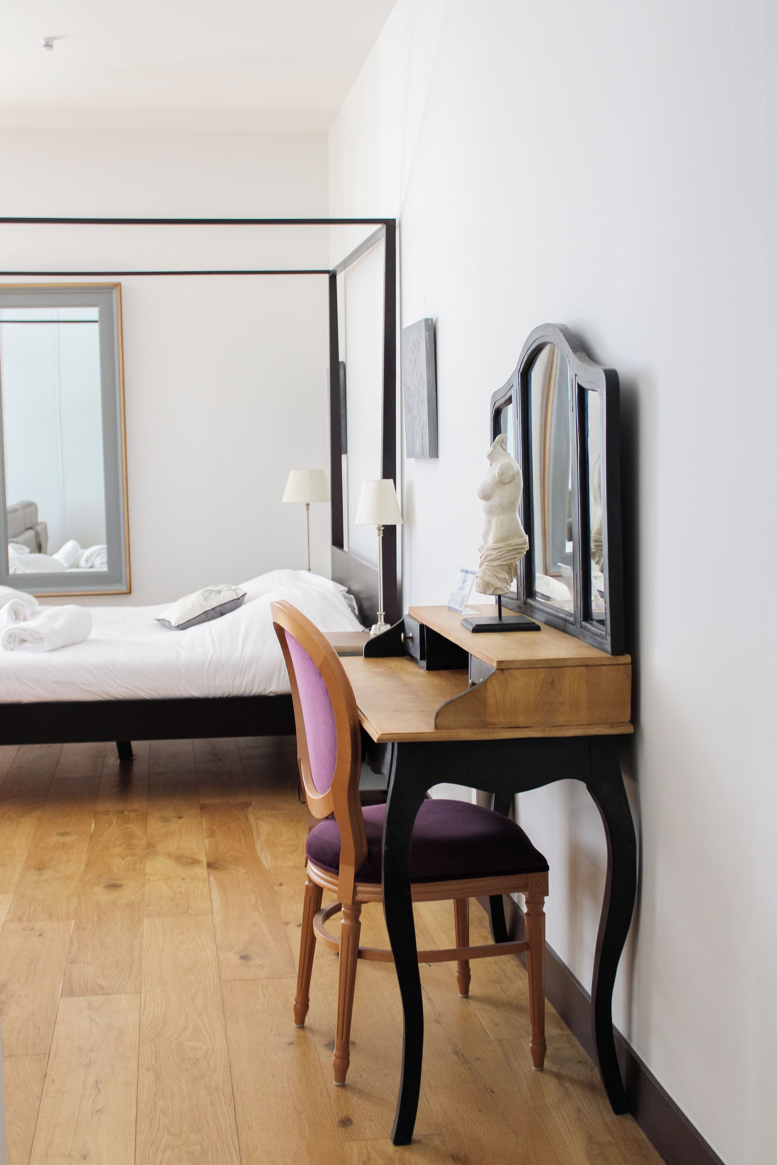 A hotel room with a bed, a desk, a chair, and a large mirror.