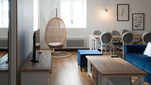Una sala de estar acogedora con un sofá azul, una mesa de centro de madera, una silla de mimbre y un comedor con mesa y sillas.