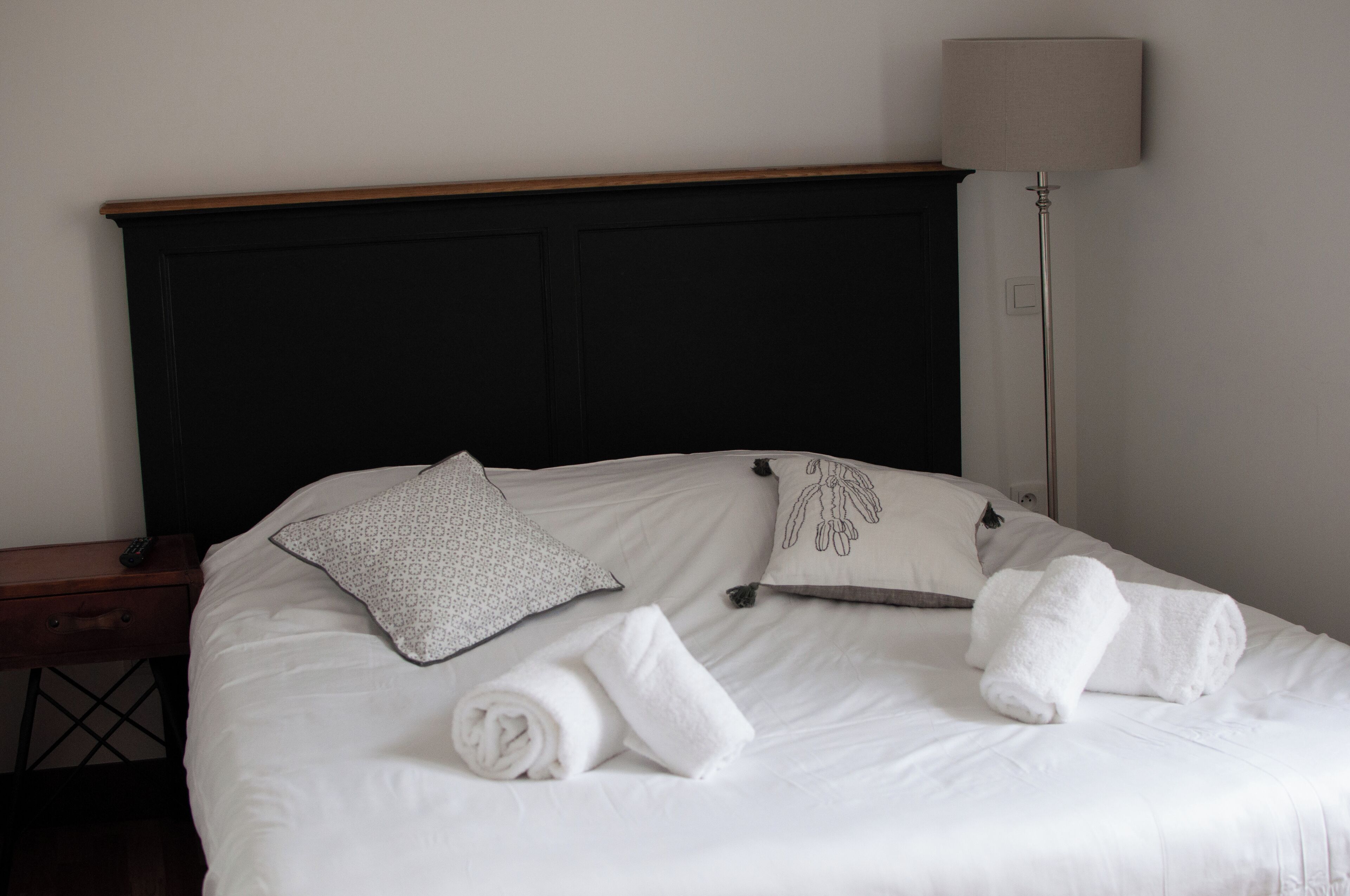 A neatly made bed with white linens, two pillows, and rolled towels.