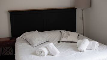 A neatly made bed with white linens, two pillows, and rolled towels.