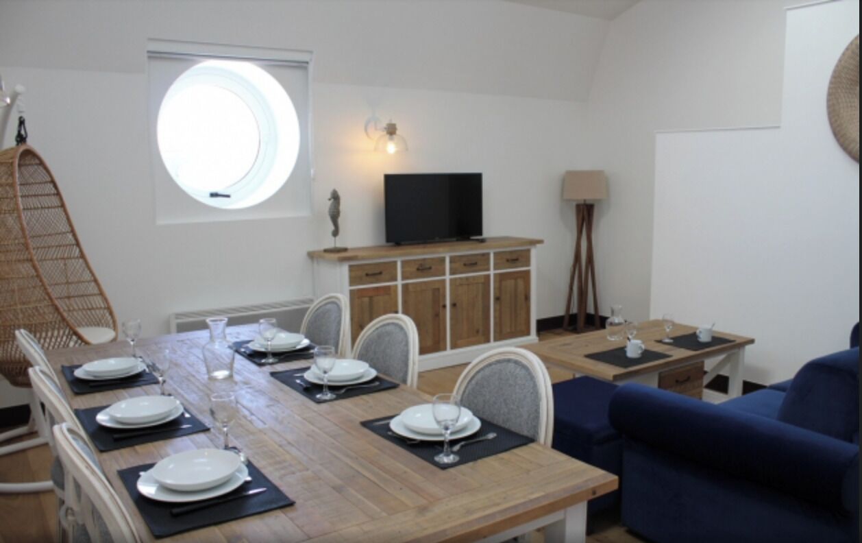 Un comedor con una mesa de madera dispuesta para cuatro personas, un televisor sobre un mueble, una lámpara y un sofá azul.