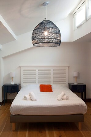 Une chambre à coucher avec un grand lit, une tête de lit blanche, deux tables de chevet avec des lampes et un luminaire suspendu.