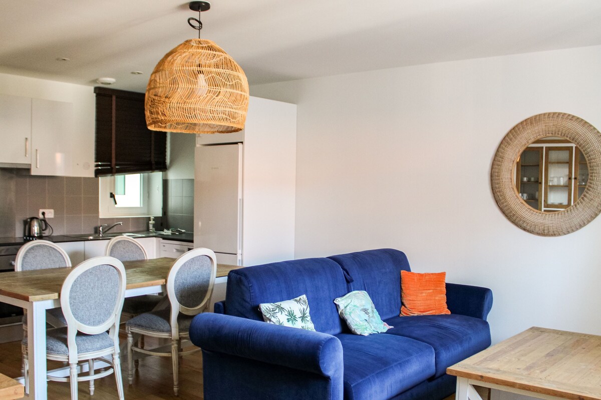 Un espacio habitable moderno con un sofá azul, una mesa de comedor, sillas y una lámpara colgante.