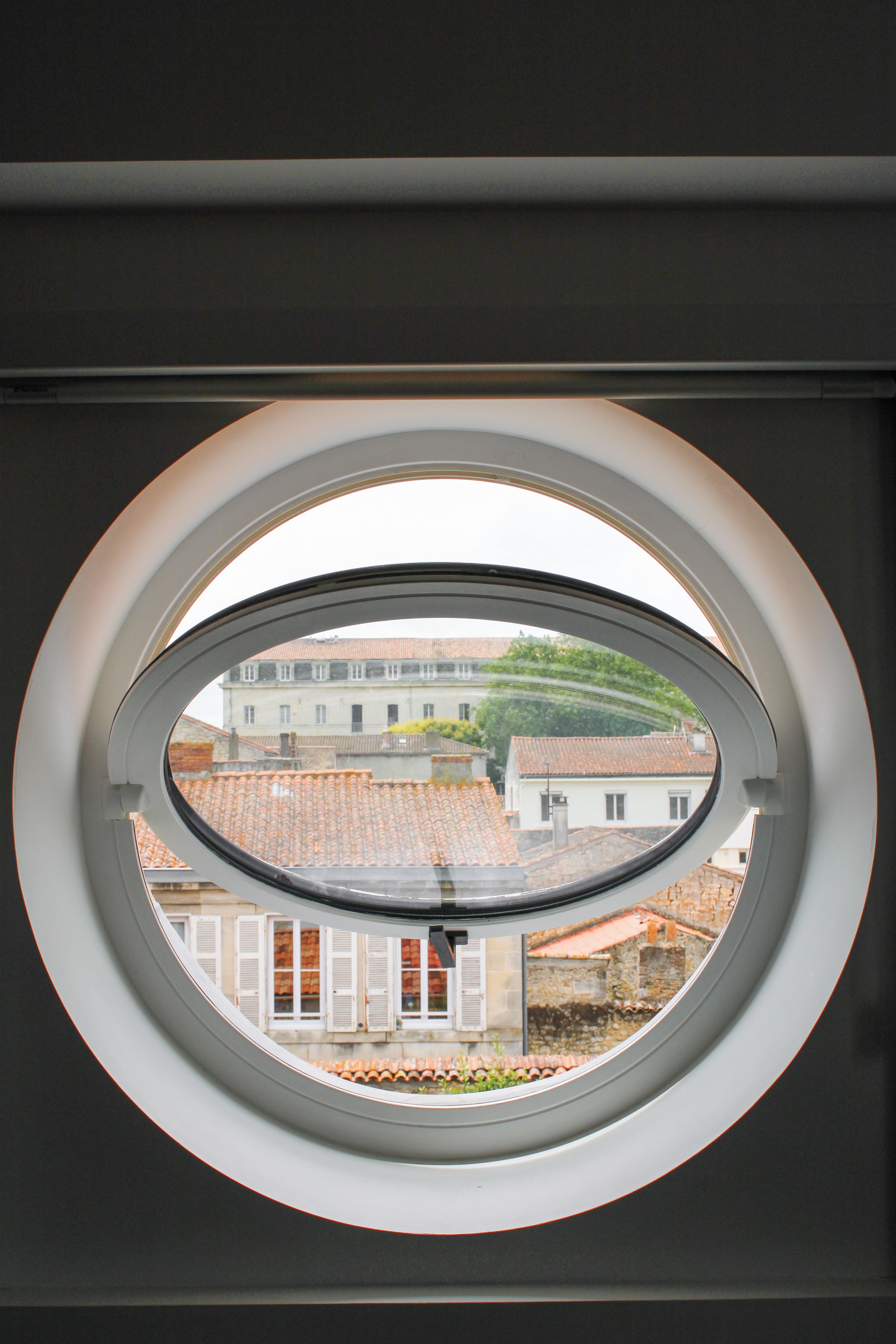 A round window with a view of buildings and a tree.