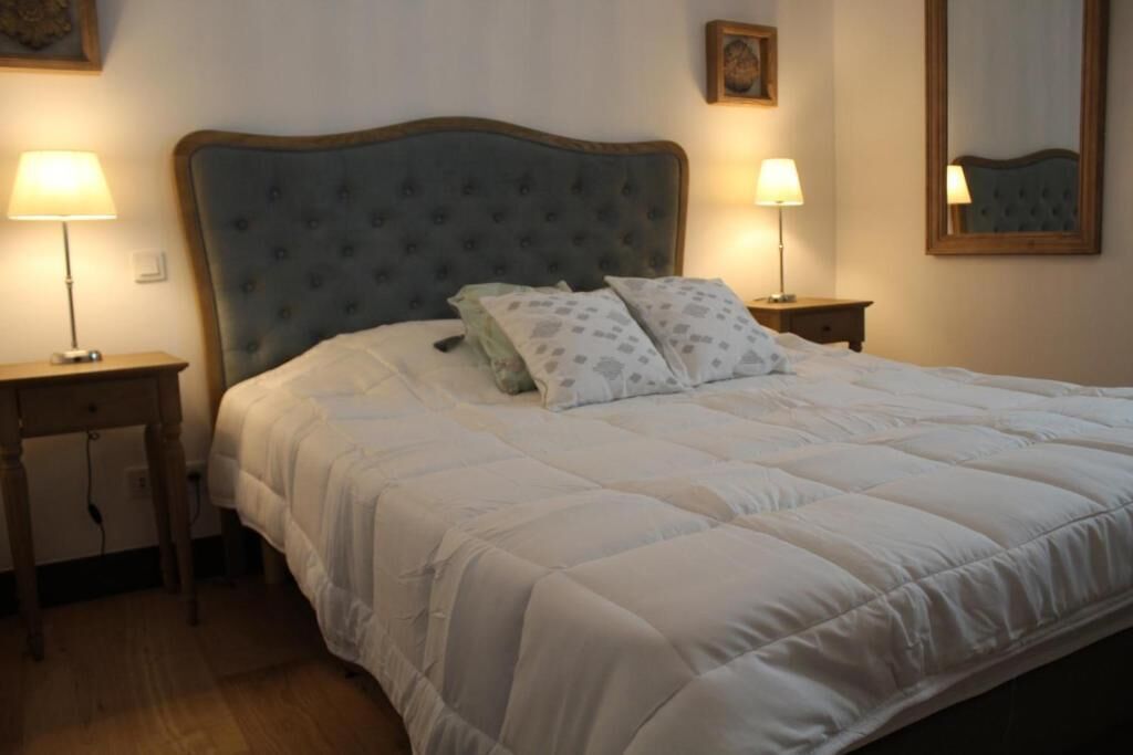 A neatly made bed with a tufted headboard, two bedside lamps, and a small bedside table.