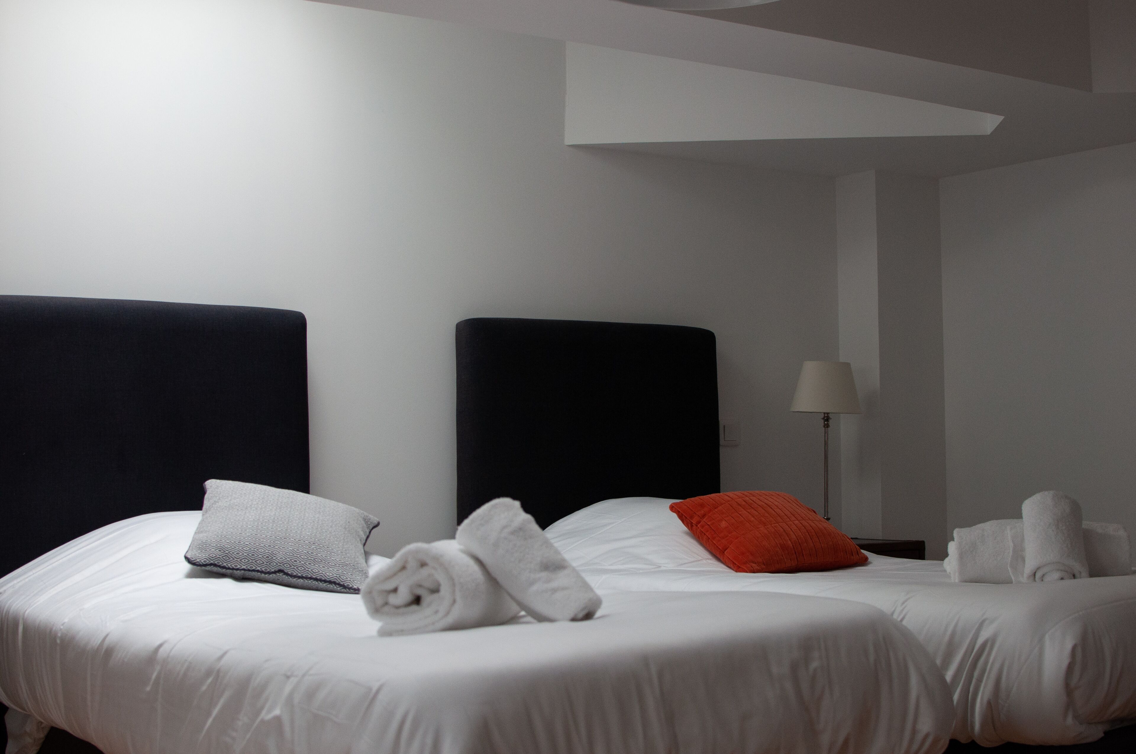 Hotellihuone, jossa on kaksi sänkyä. Jokaisessa sängyssä on valkoiset lakanat ja tyynyt, sekä lamppu ja siististi taitetut pyyhkeet.