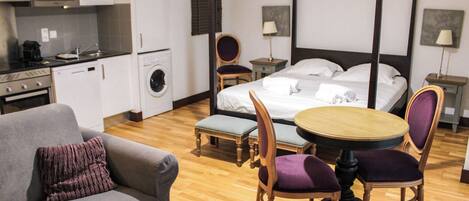 A hotel room with a bed, a dining table with chairs, a sofa, a washing machine, and a microwave.
