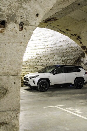 Ein weißer SUV steht unter einer Bogenkonstruktion aus Stein.