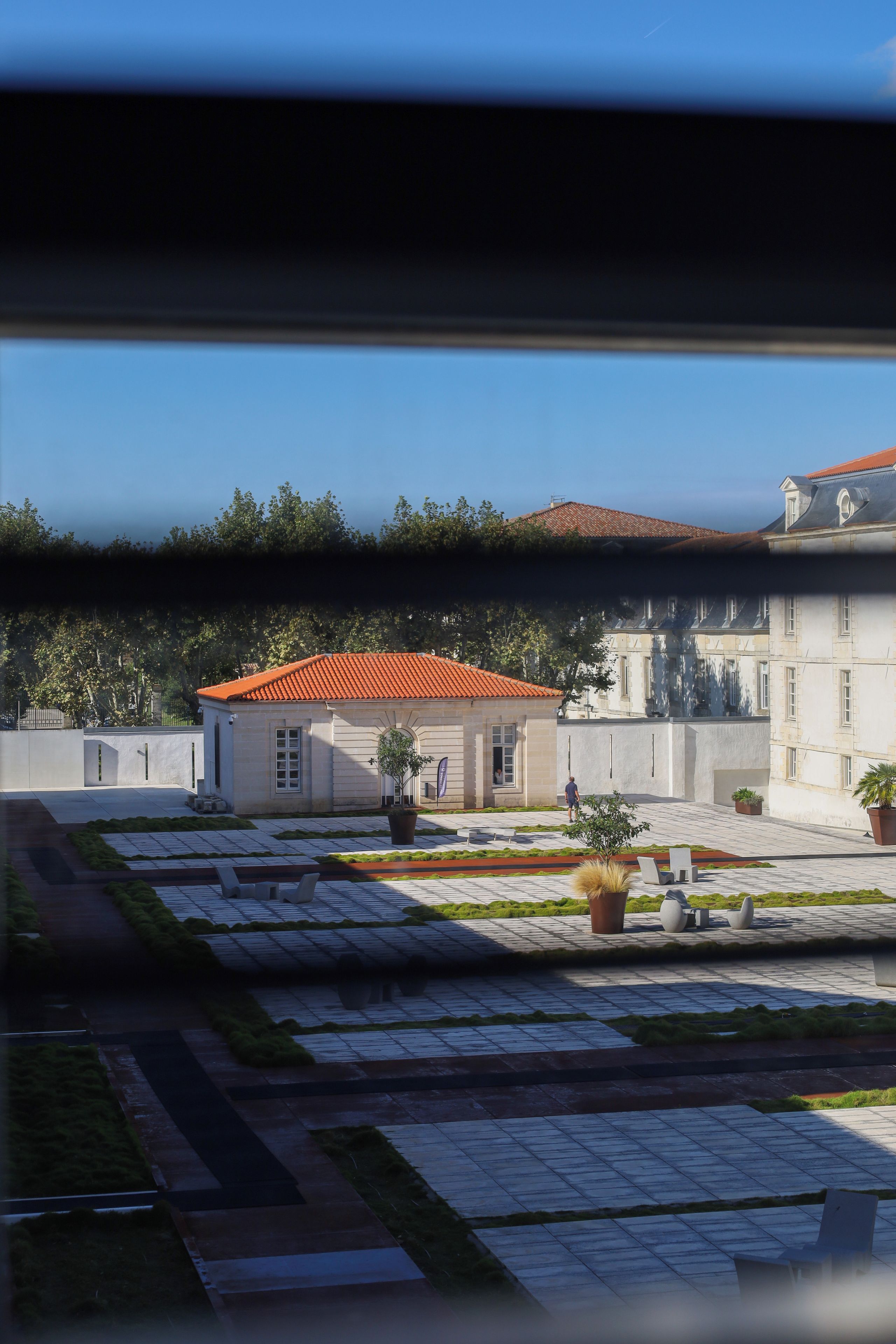 Un patio con un edificio que tiene techo de tejas rojas, plantas en macetas y un área de estar con bancos.