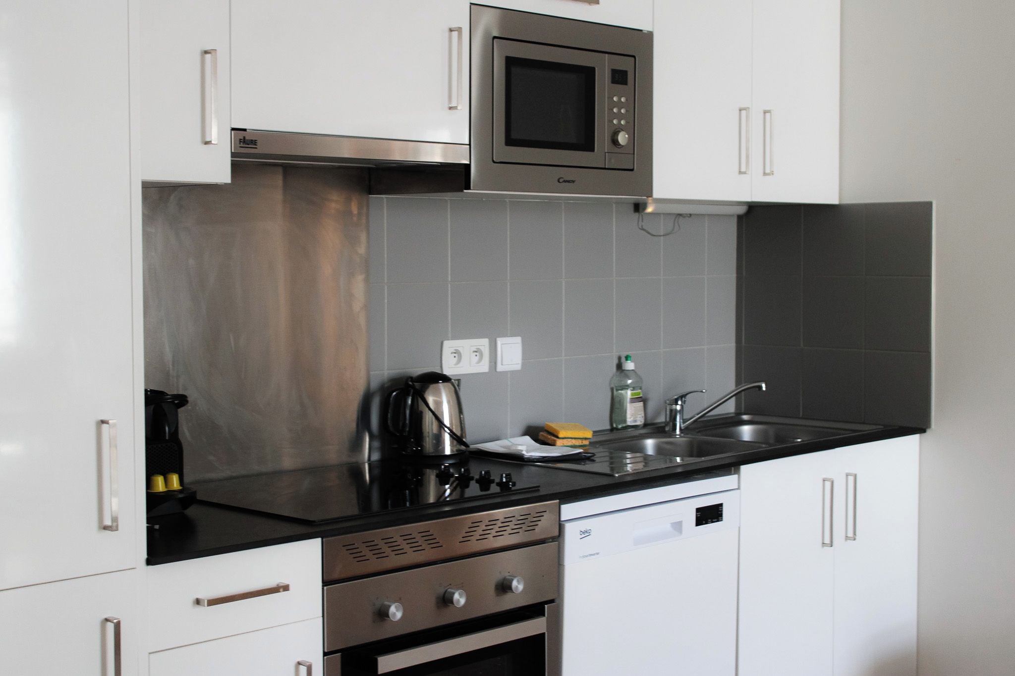 Een moderne keuken met roestvrijstalen apparatuur, een zwart aanrecht en witte kastjes.