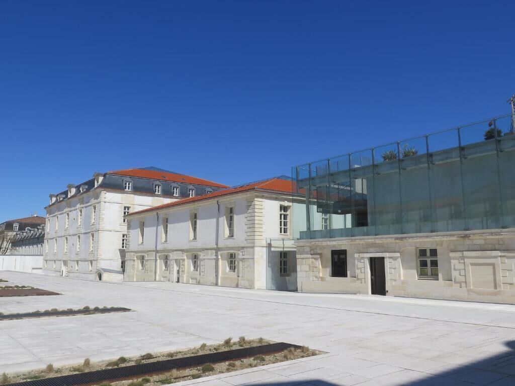 Ein historisches Gebäude mit einem modernen Glasanbau, einem gepflasterten Innenhof und blauem Himmel.
