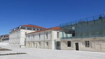 Ein historisches Gebäude mit einem modernen Glasanbau, einem gepflasterten Innenhof und blauem Himmel.