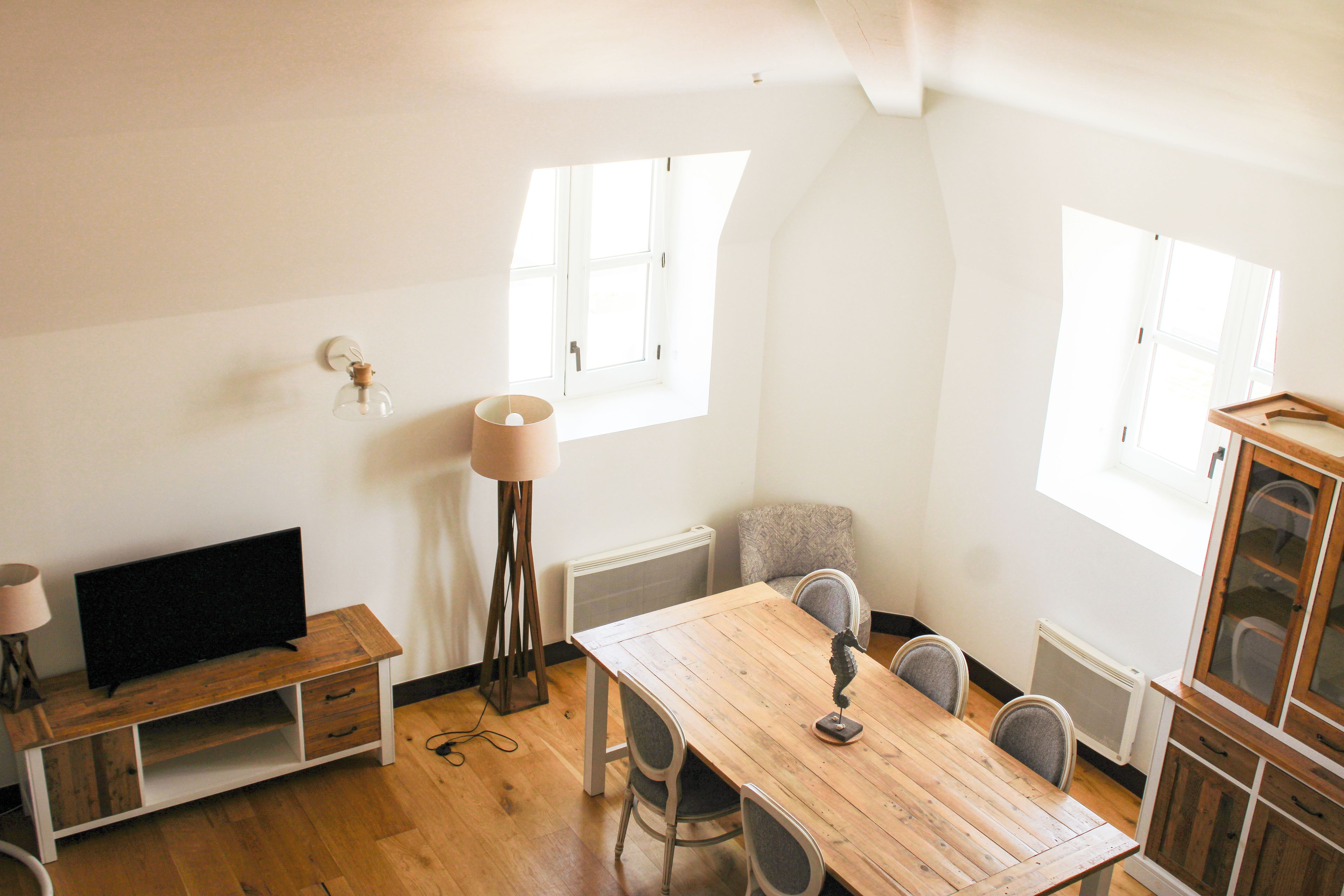 A dining area with a wooden table, chairs, a floor lamp, and a television on a stand.