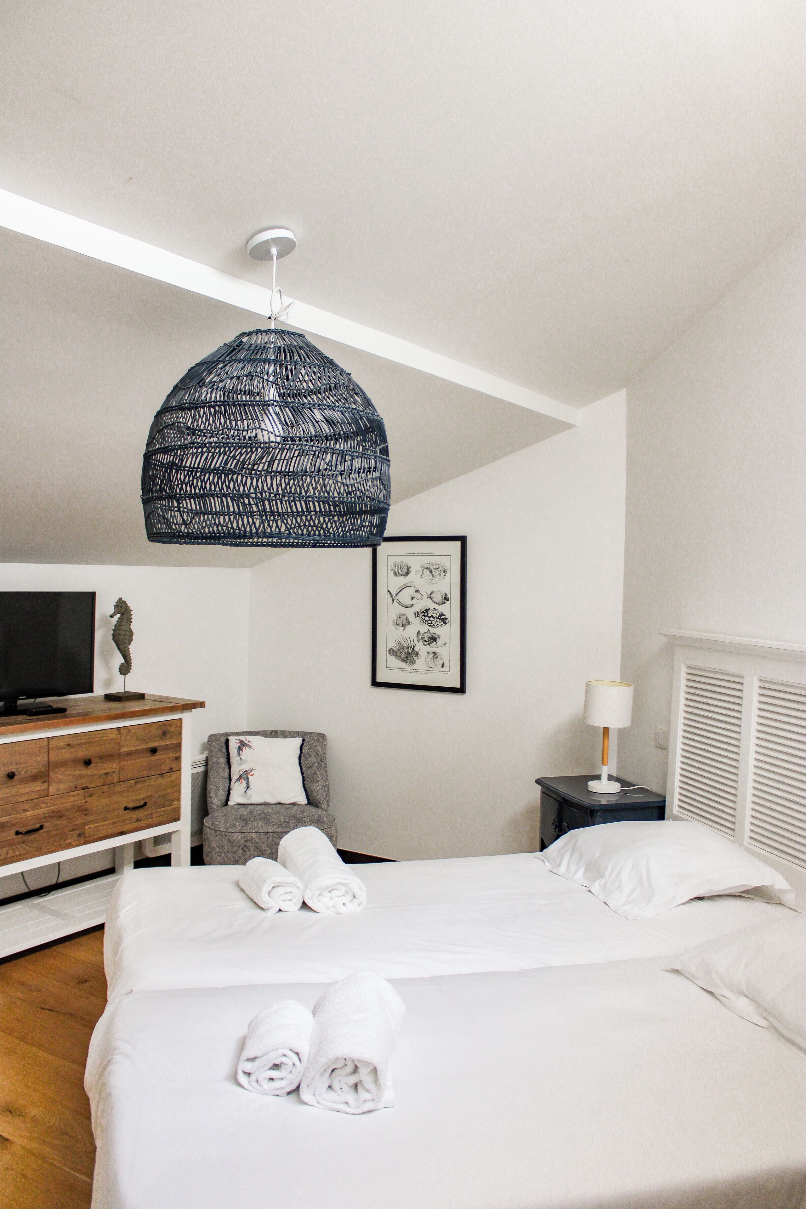 Habitación de hotel con una cama, un escritorio con televisor, una silla, un cuadro en la pared y una lámpara colgante.