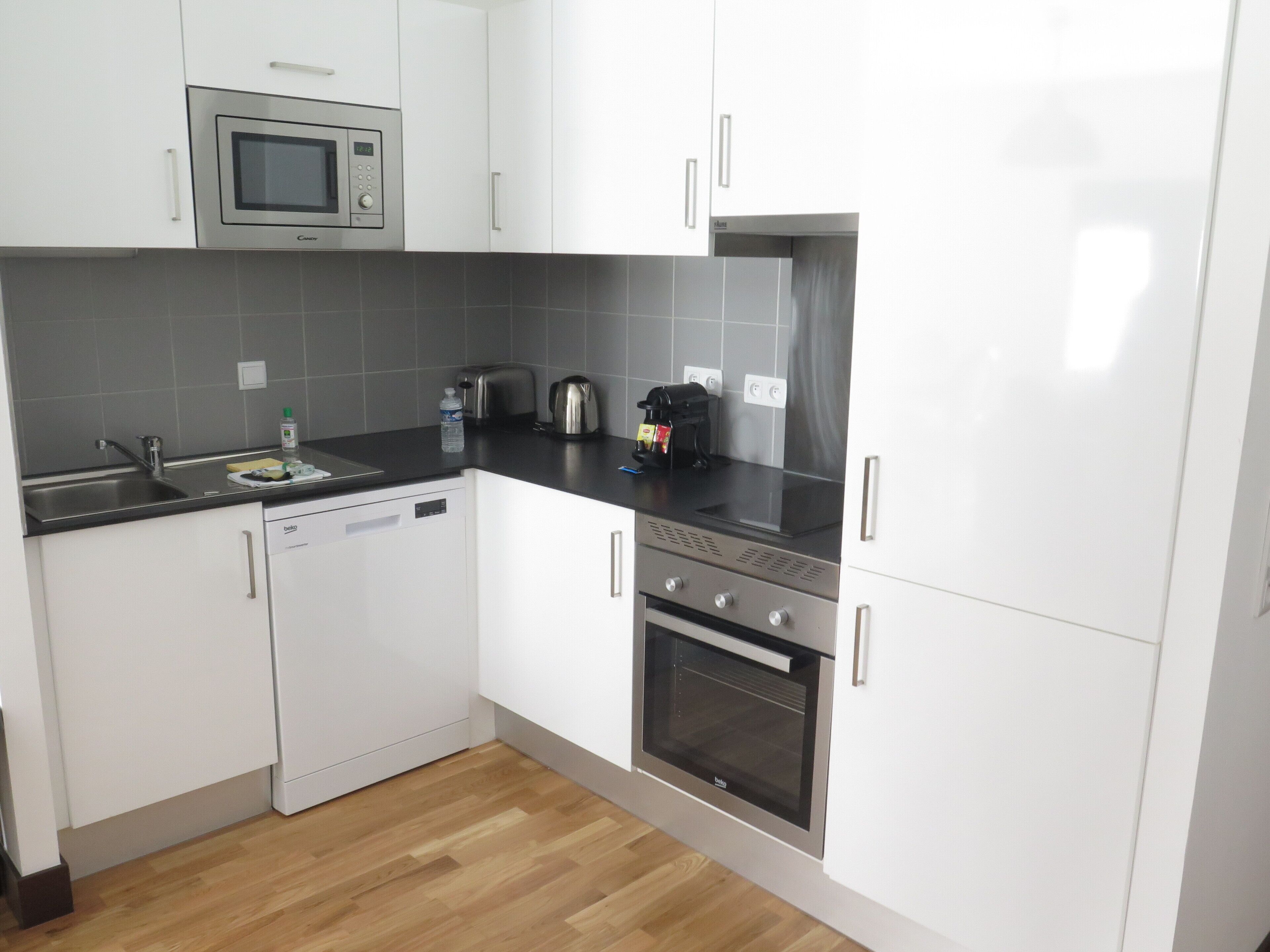 Una cocina moderna con armarios blancos, un microondas de acero inoxidable, un tostador y un lavavajillas.