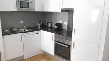 Una cocina moderna con armarios blancos, un microondas de acero inoxidable, un tostador y un lavavajillas.