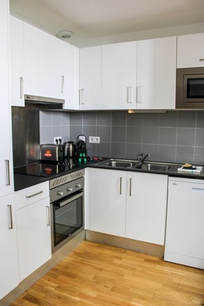 A modern kitchen with white cabinets, stainless steel appliances, and a wooden floor.