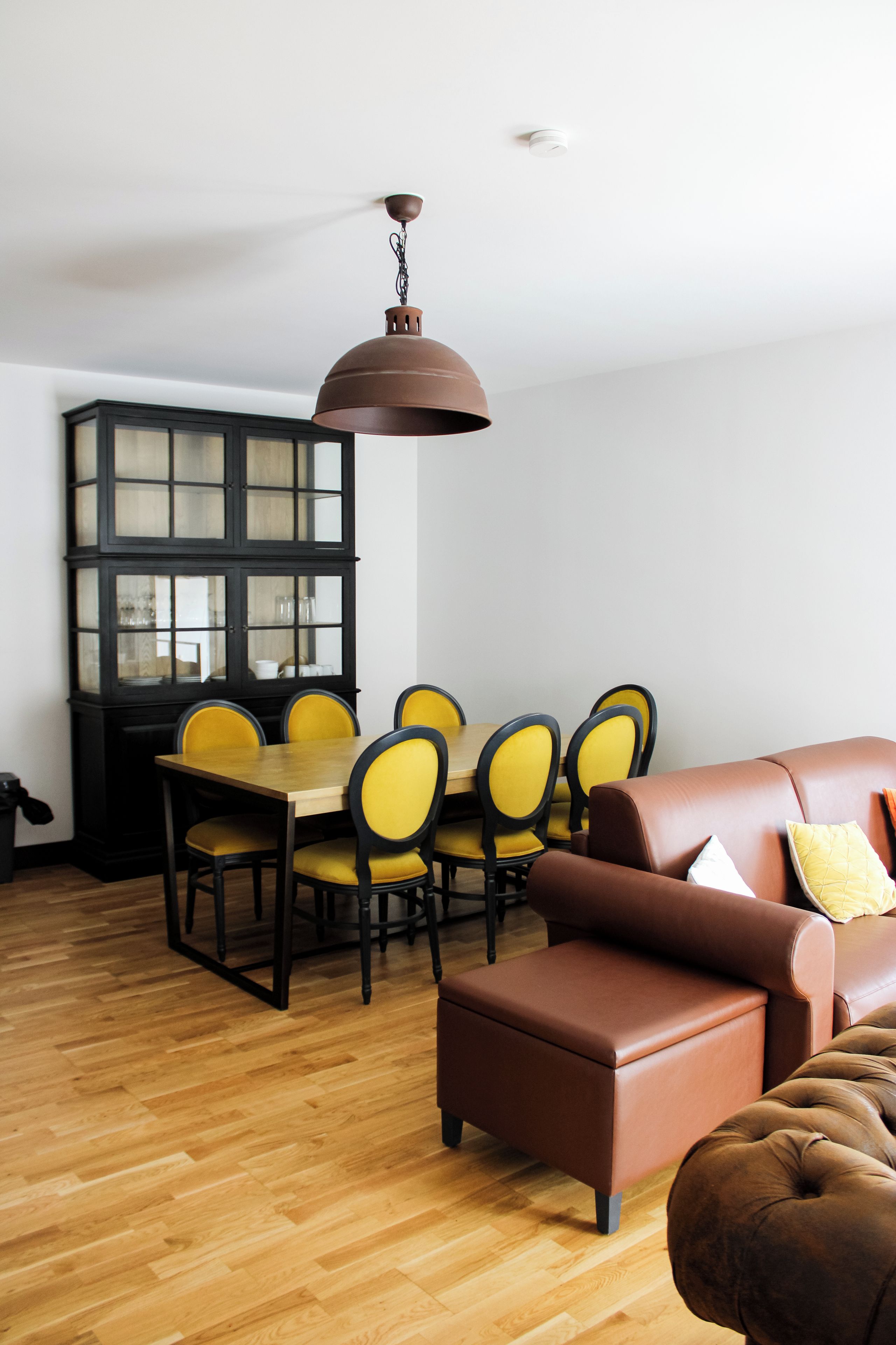 A dining area with a wooden table and chairs, a black cabinet, and a brown leather sofa.