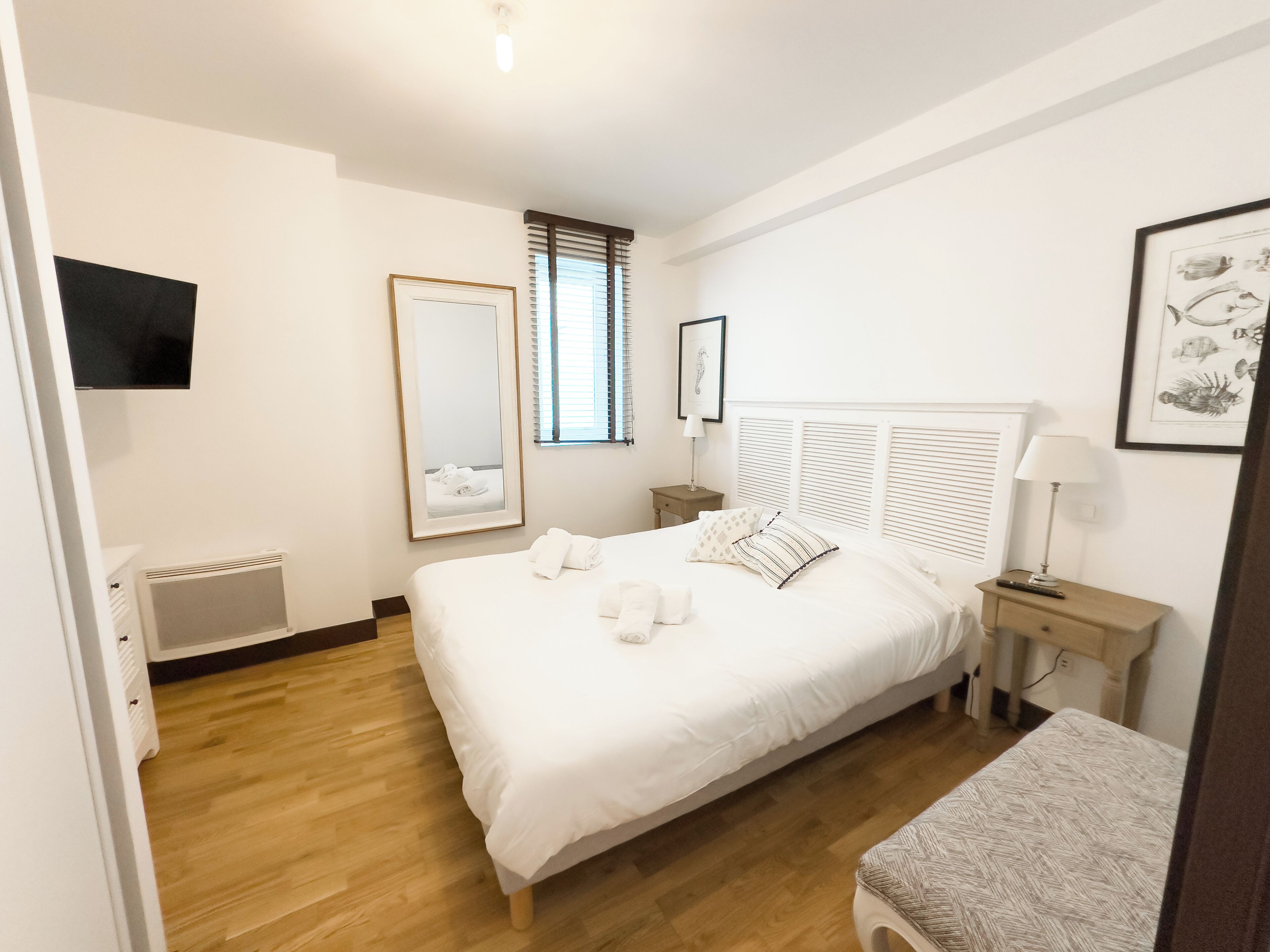 Ein Hotelzimmer mit einem großen Bett, einem Nachttisch, einer Lampe, einem Spiegel und einem gerahmten Bild an der Wand.