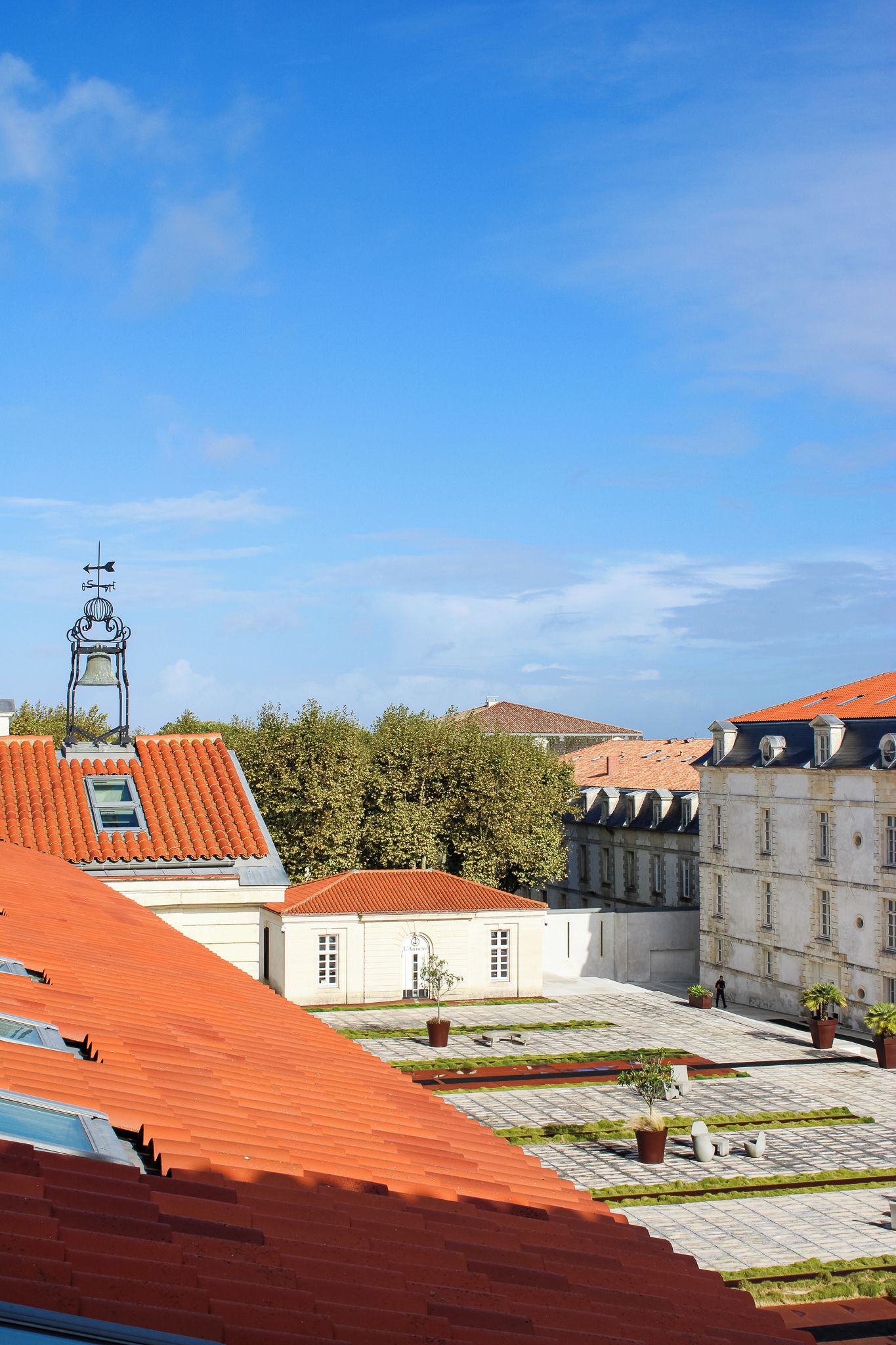 A courtyard with red-tiled roofs, a bell tower, and a building with a white facade.