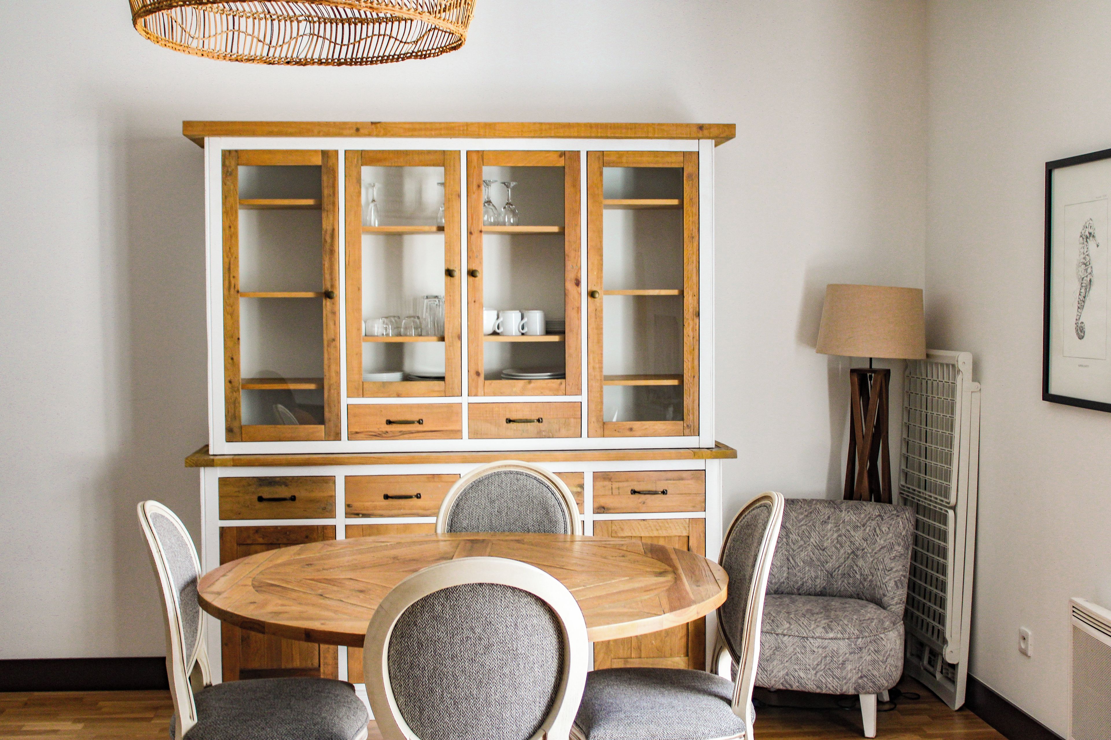 A dining area with a wooden table and chairs, a cabinet with glass doors, and a lamp.