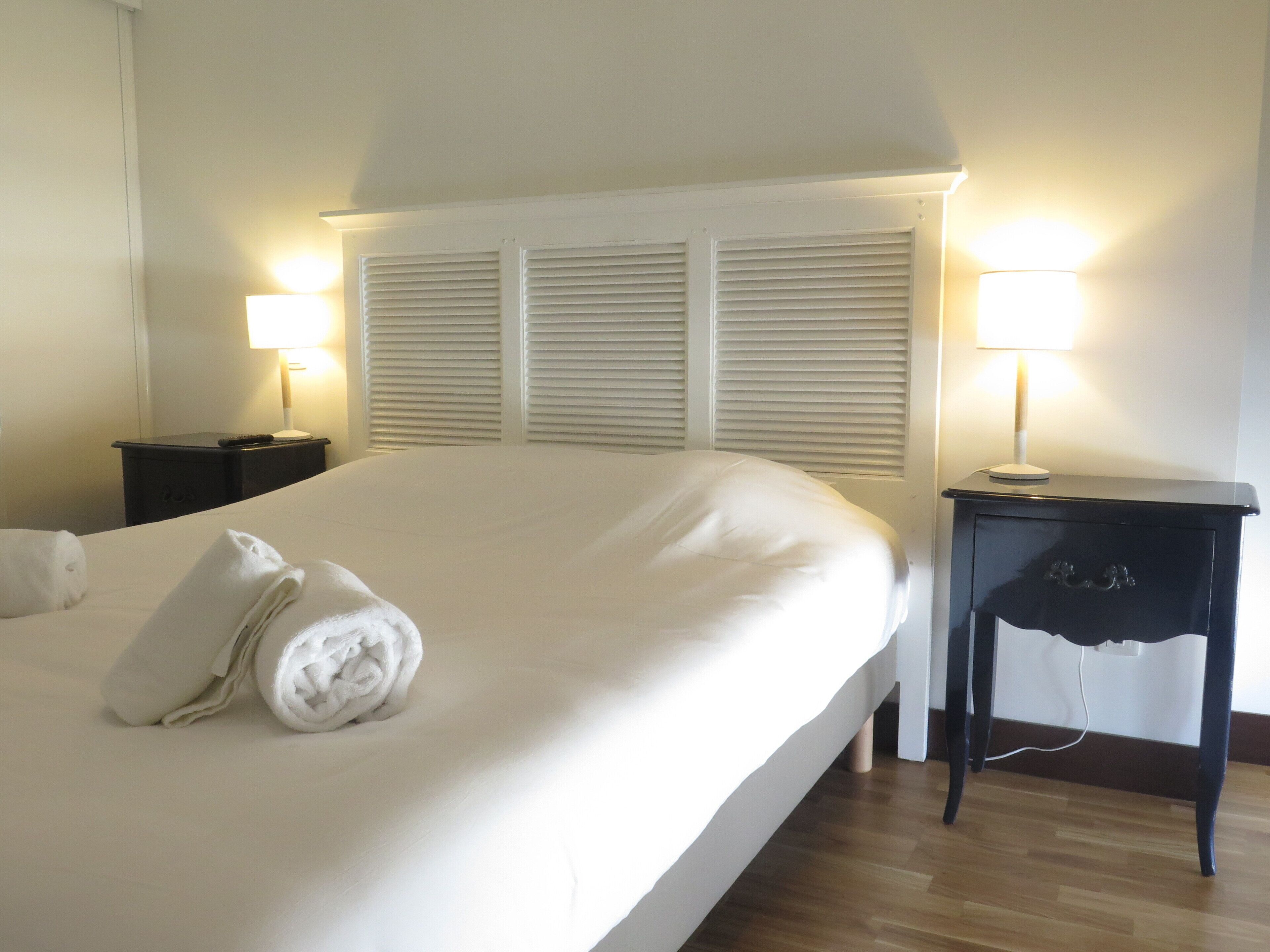 A hotel room with a large bed, two bedside tables, and a nightstand with a lamp.