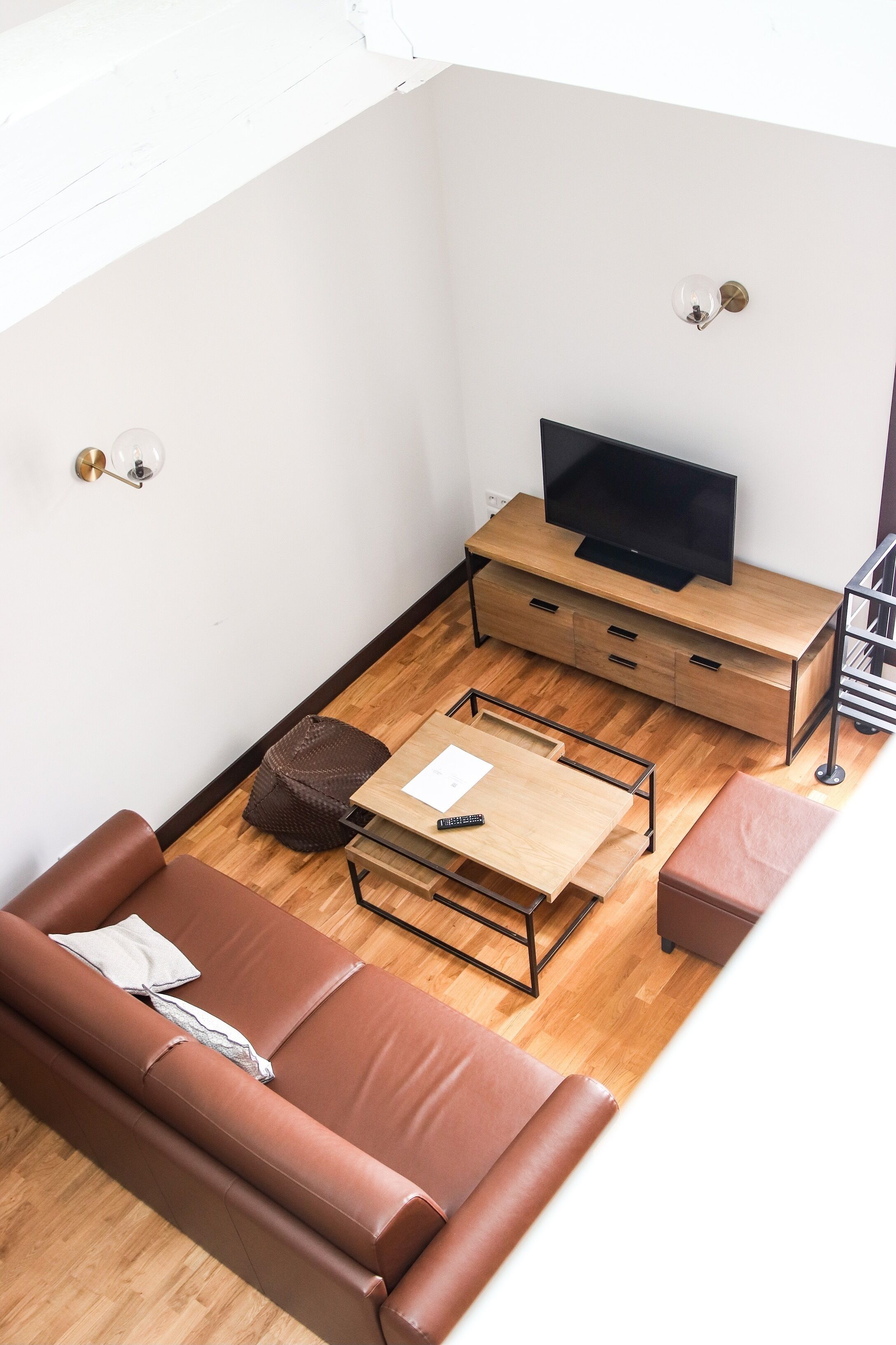 Un espai habitable compacte amb un sofà de cuir marró, una taula de centre de fusta, una televisió sobre un suport de fusta i una taula auxiliar petita.