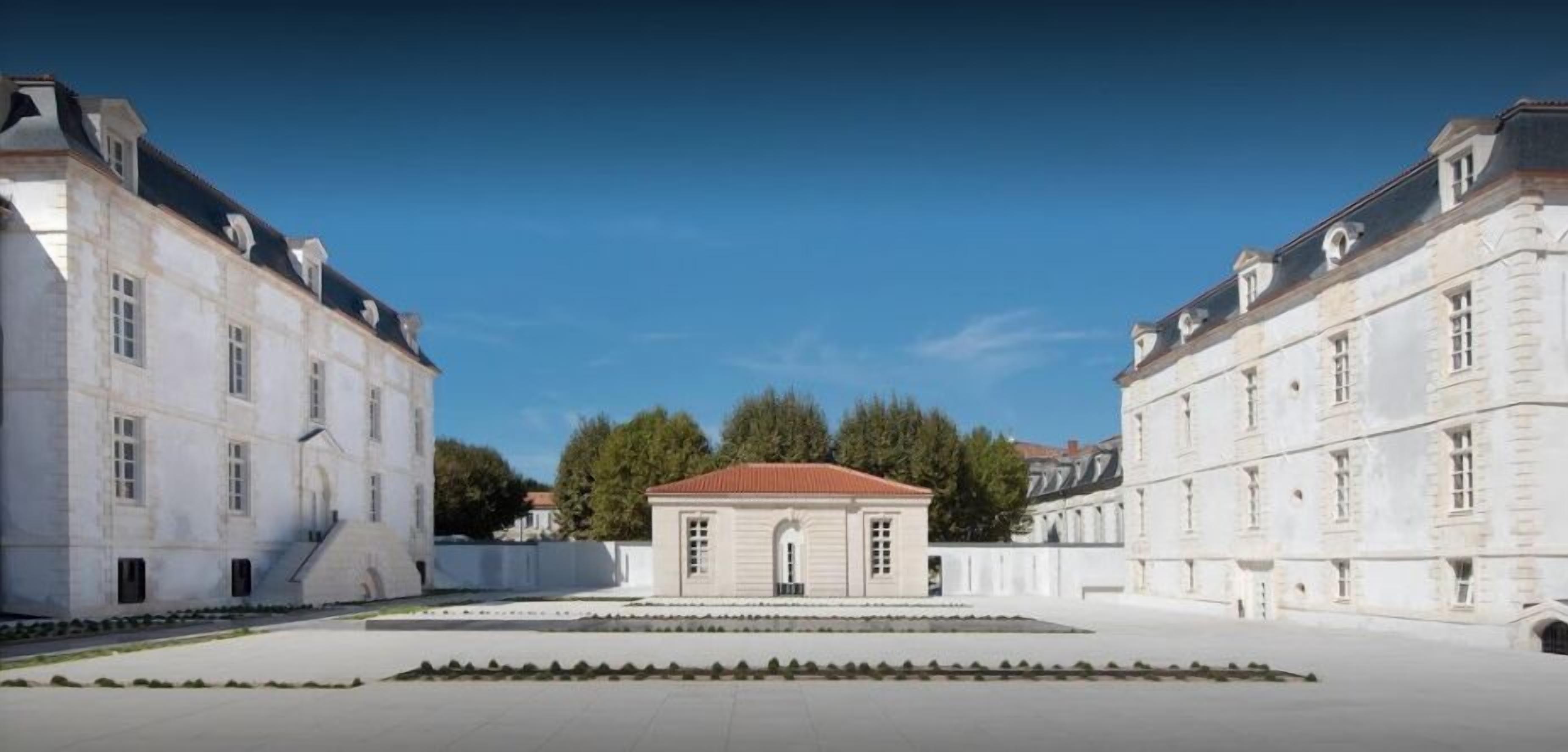 A courtyard with a central building featuring a red roof, flanked by two large white buildings with classical architecture.