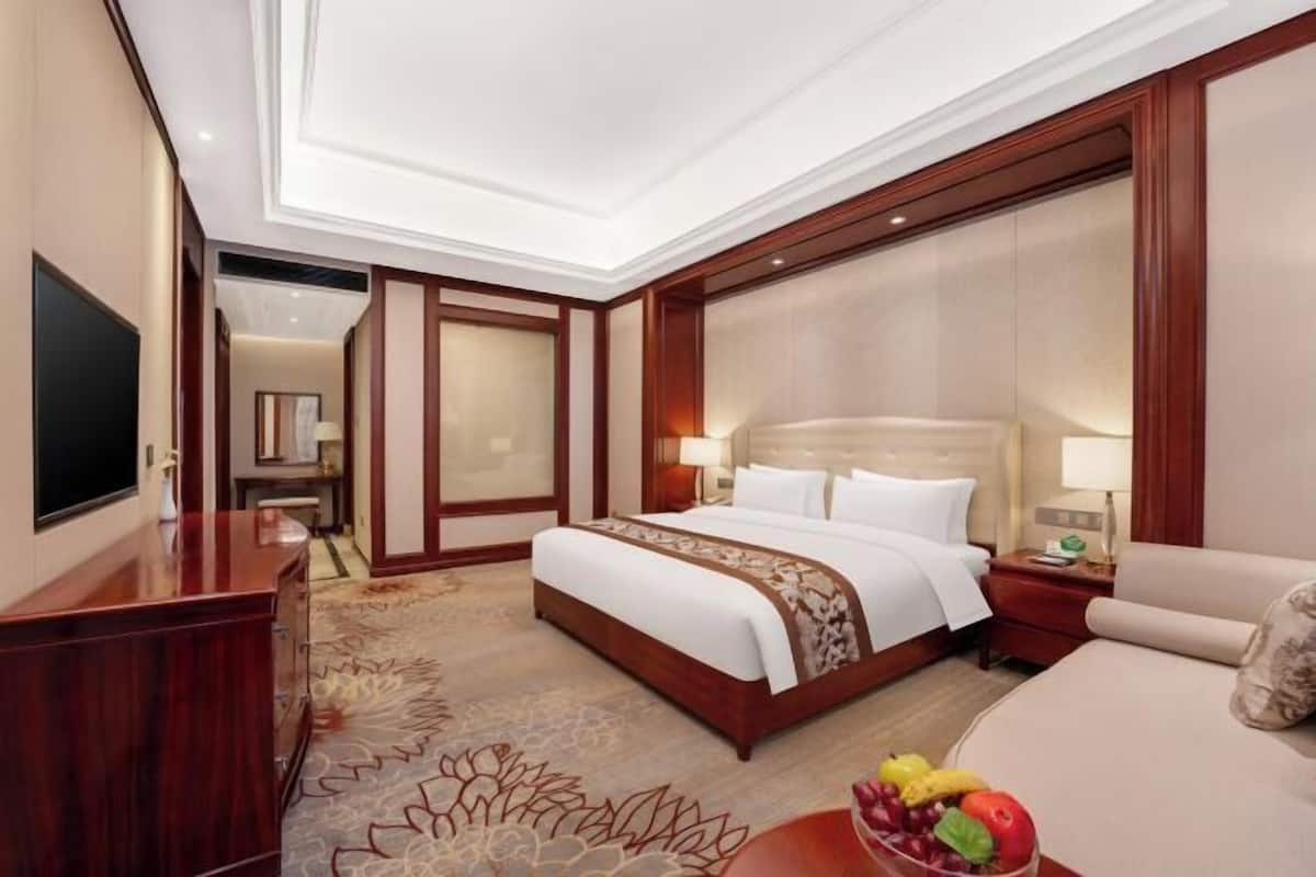 Habitación de hotel con una cama grande, un escritorio, un televisor y un frutero en la mesita de noche.