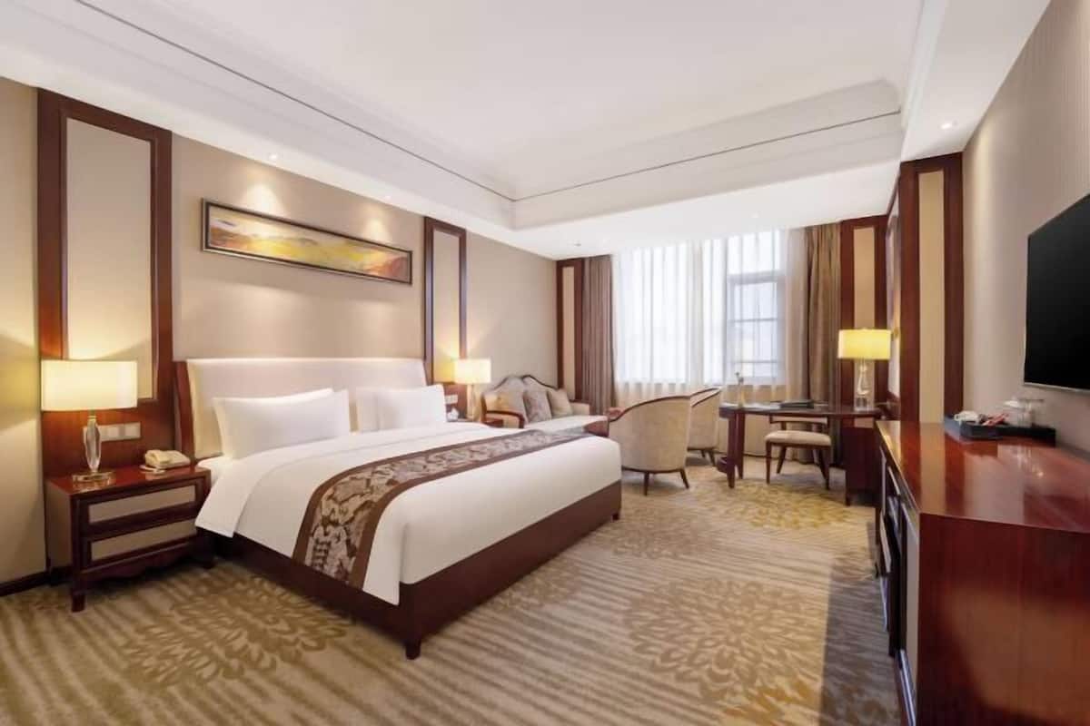 Habitación de hotel con una cama grande, un escritorio, una silla, un televisor y una ventana con cortinas.