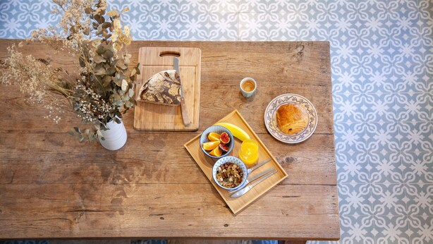 A wooden table with a fruit bowl, a plate of food, a vase with dried flowers, and a cutting board with a knife. - Lyonest Chambre D'hôtes (Lyon)