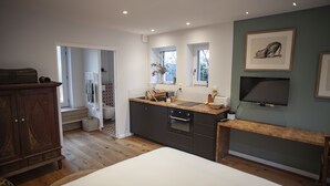 A modern kitchen with wooden cabinets, a built-in oven, and a sink. There is a wooden bench and a framed picture on the wall. - Lyonest Chambre D'hôtes (Lyon)