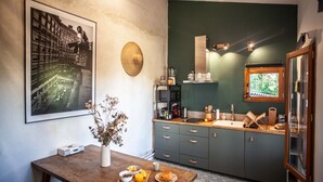 A kitchen with a green wall, a framed photograph, a wooden table with breakfast items, and a window with a view of greenery. - Lyonest Chambre D'hôtes (Lyon)