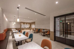 Un restaurante moderno con mesas comunes largas y cabinas, iluminación colgante y vistas de la ciudad a través de amplias ventanas.