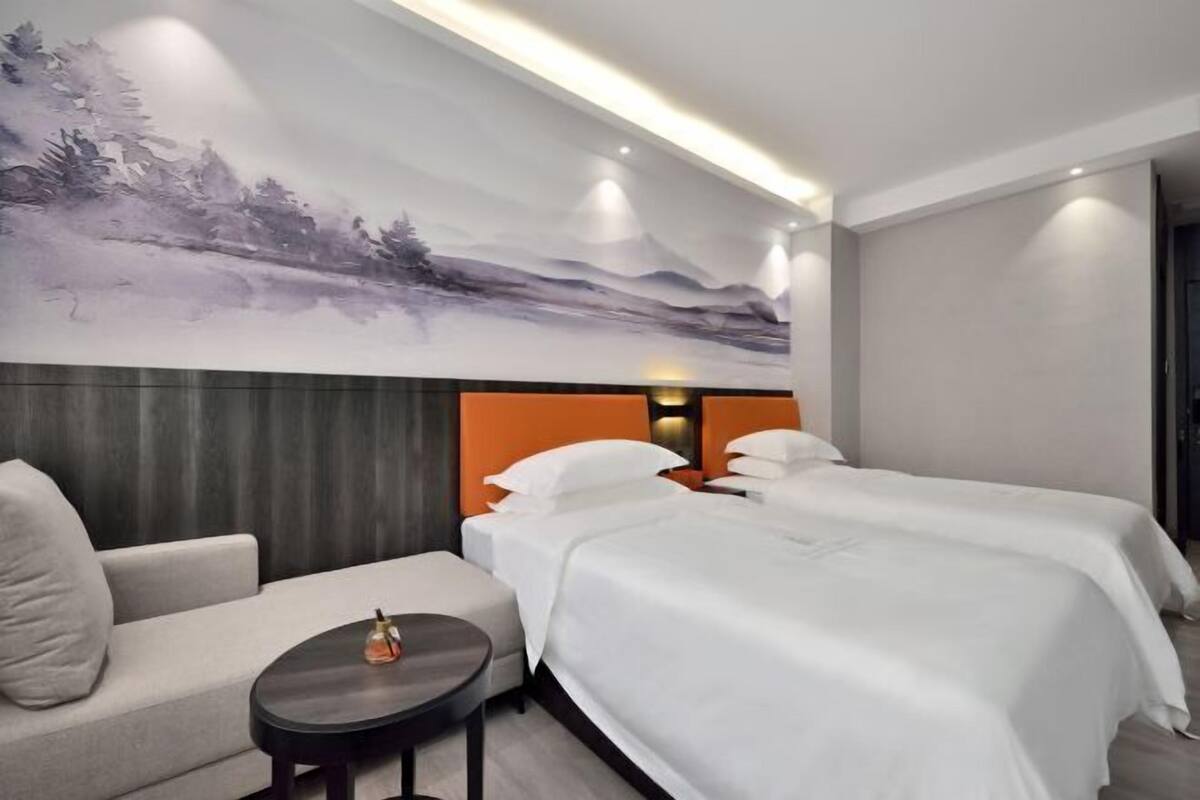 A hotel room with two beds, a sofa, a small table, and a large wall mural.