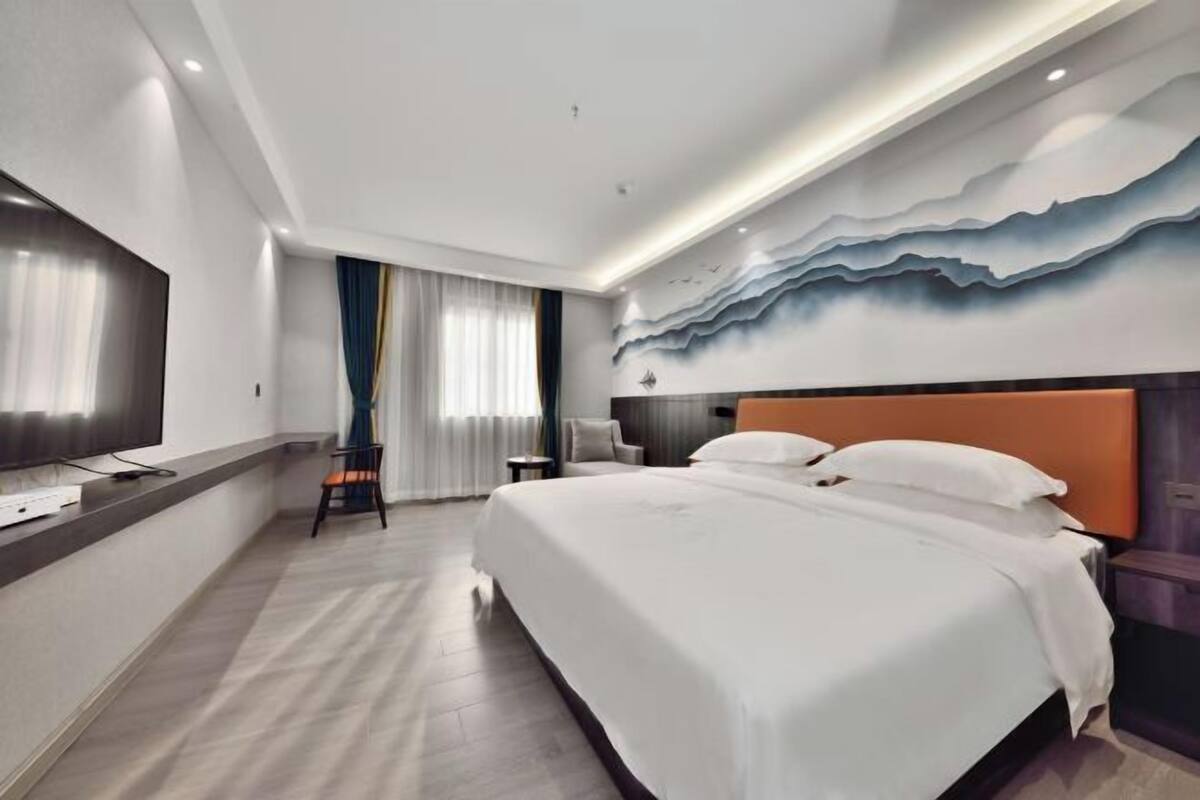 A modern hotel room with a large bed, a flat-screen TV, and a wall mural.