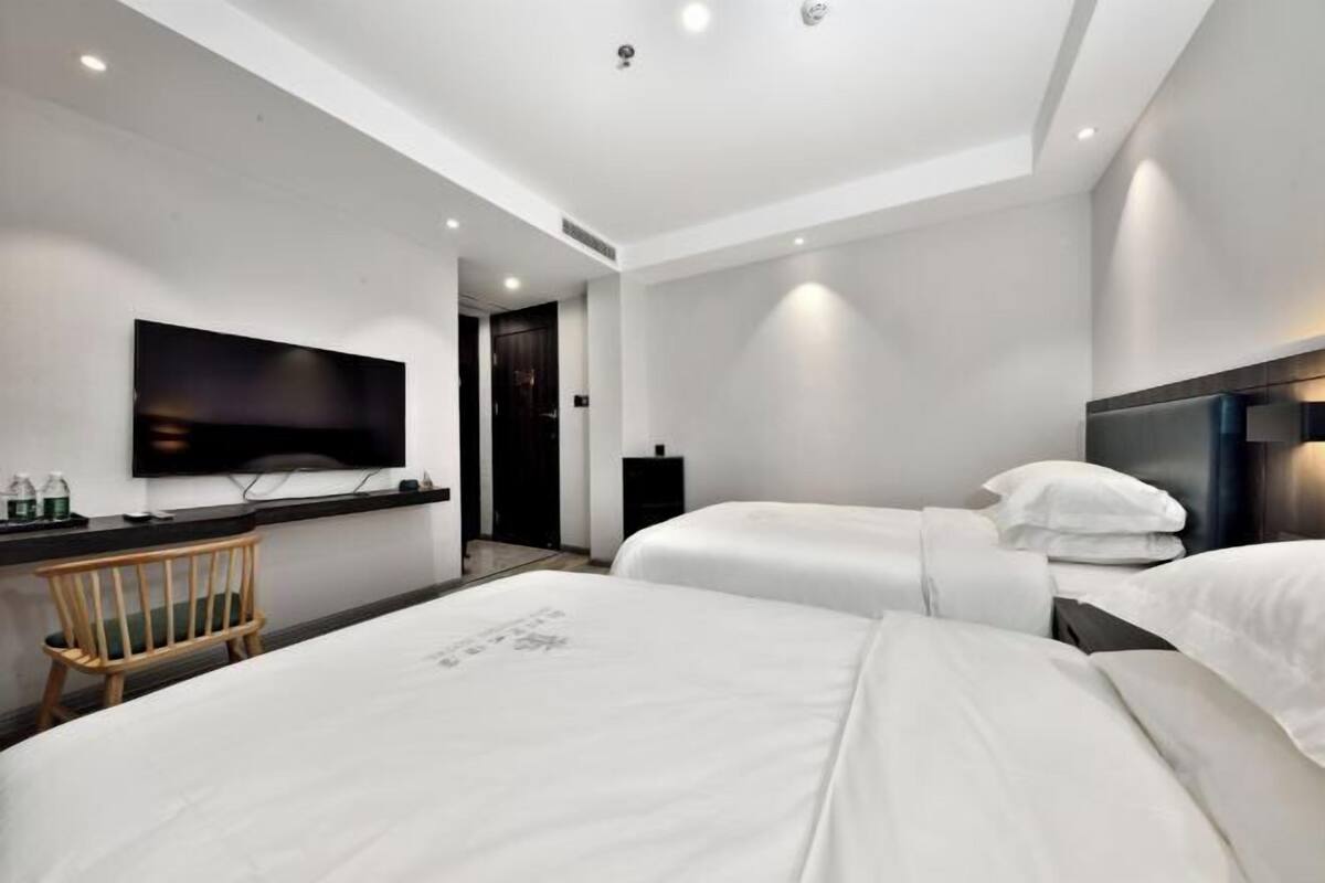 A hotel room with two beds, a flat-screen TV mounted on the wall, a wooden chair, and a desk with a lamp.